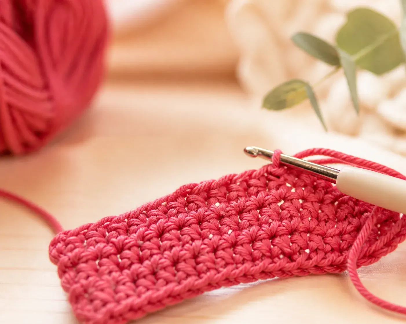 Macro d'un rang de mailles serrées en coton framboise en cours de réalisation, le crochet encore engagé dans la maille
